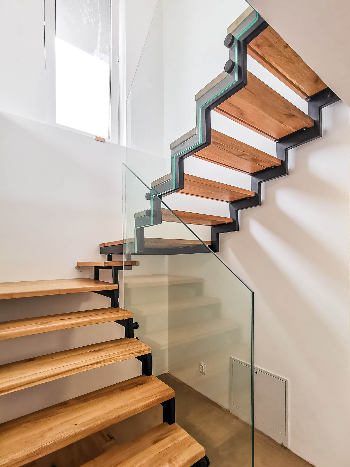 sklenené zábradlie ukotvené do oceľovej konštrukcie s drevenými stupnicami a atypickým výrezom podľa schodov