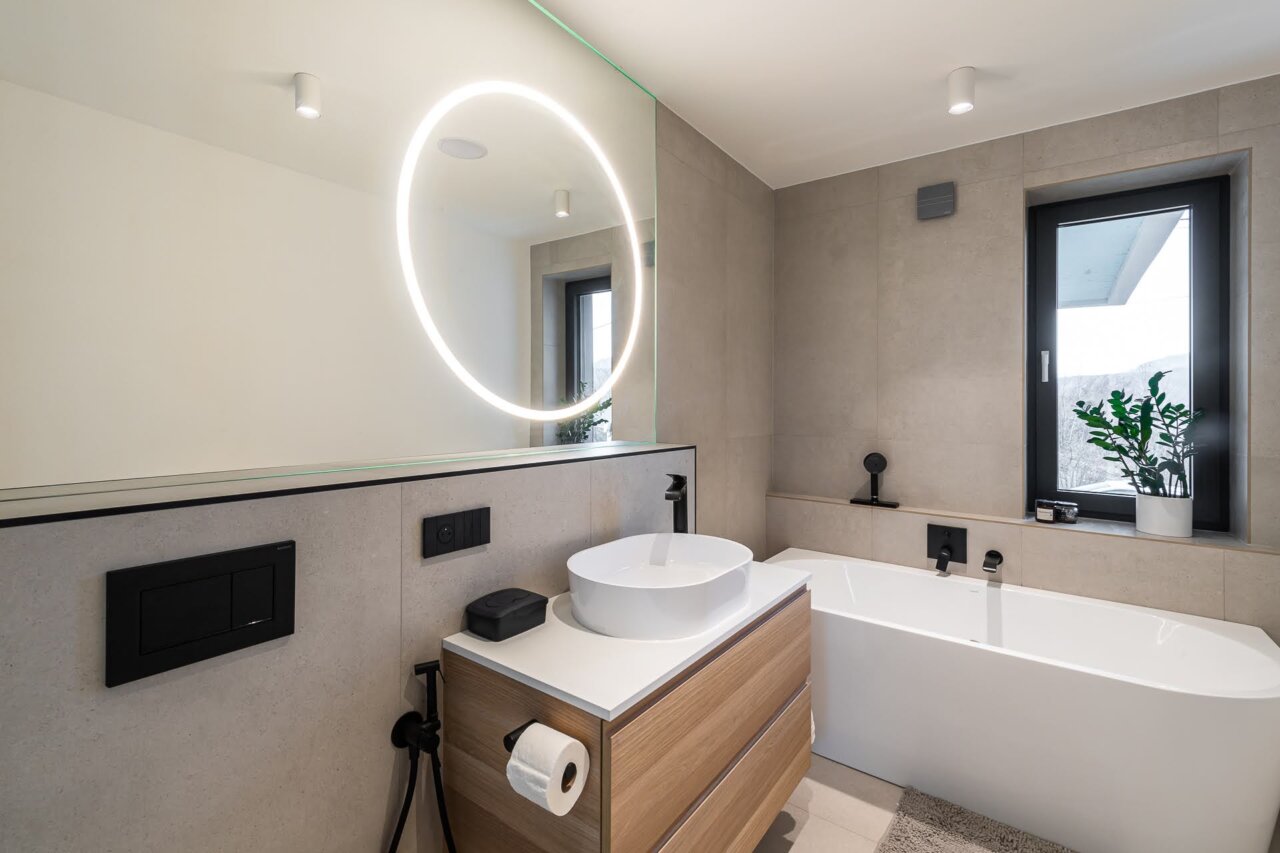 Okrúhle LED zrkadlo s integrovaným svetlom nad umývadlom v kúpeľni s matným skleneným obkladom.
